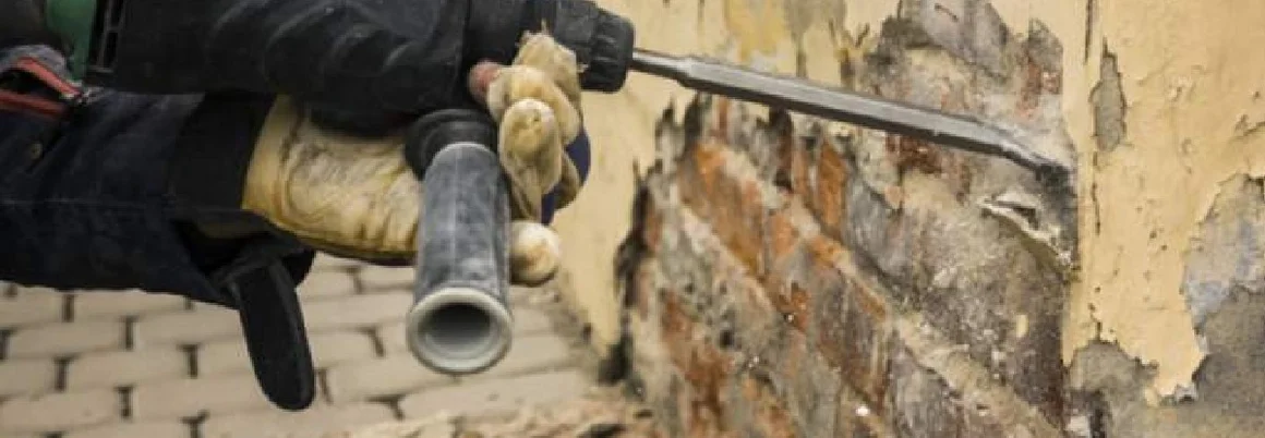 Person mit Meißel entfernt Putz von Wand